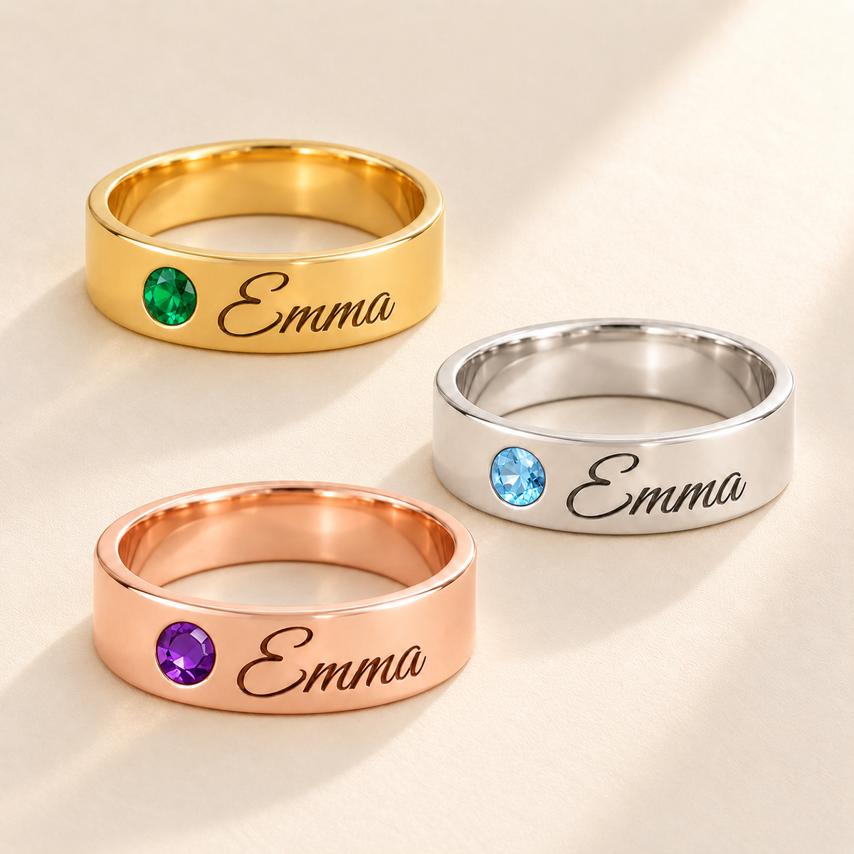 Custom Wide Band Name Ring with Birthstone glamour photo - three polished wide name rings in gold emerald, silver Blue Topaz and rose gold amethyst on pale ivory Anthology Jewelry