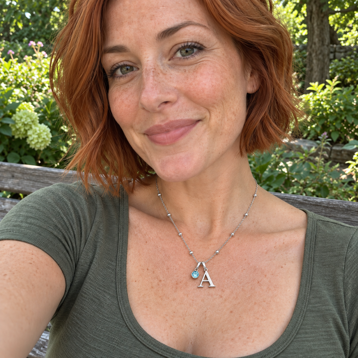 Custom Birthstone Initial Necklace UGC photo - silver serif A with March pale blue birthstone worn on a garden bench Anthology Jewelry