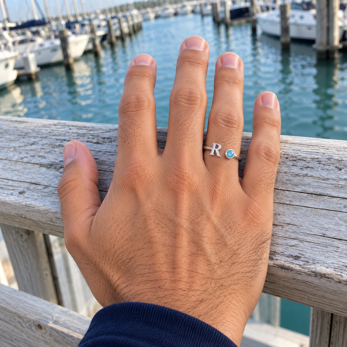 Custom Open Birthstone Initial Ring UGC photo - silver R and March pale blue birthstone on a relaxed hand resting on a harbor railing Anthology Jewelry