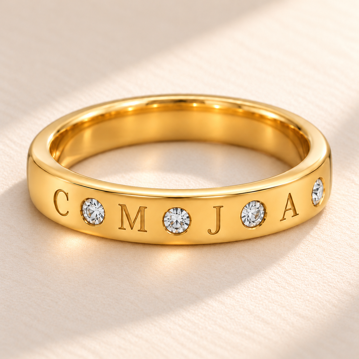 Close-up of four engraved initials C M J A and four flush-set clear stones