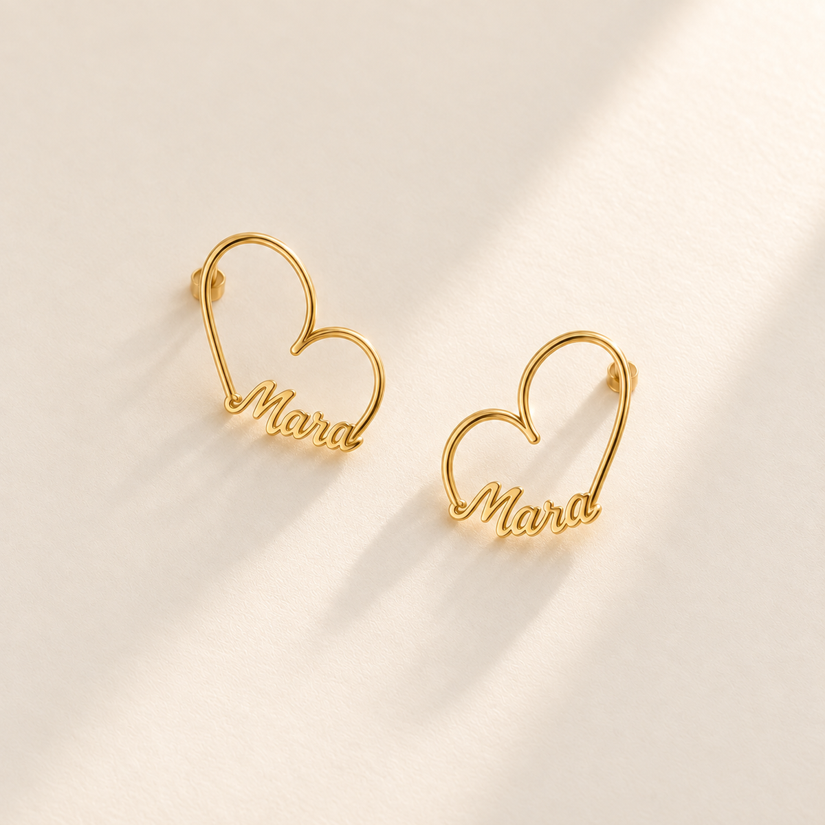 Custom Heart-Frame Name Stud Earrings gold hero on pale ivory background - Anthology Jewelry