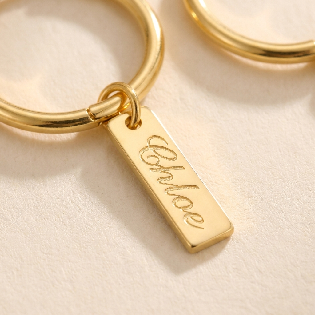 Custom Nameplate Huggie Hoop Earrings detail photo - macro closeup of engraved dangling gold charm and hoop hinge Anthology Jewelry