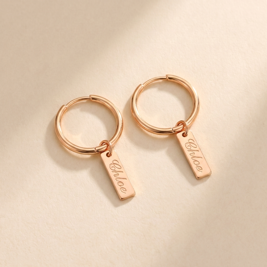 Custom Nameplate Huggie Hoop Earrings hero photo - rose gold huggie hoop earrings with engraved nameplate charm on cream background Anthology Jewelry