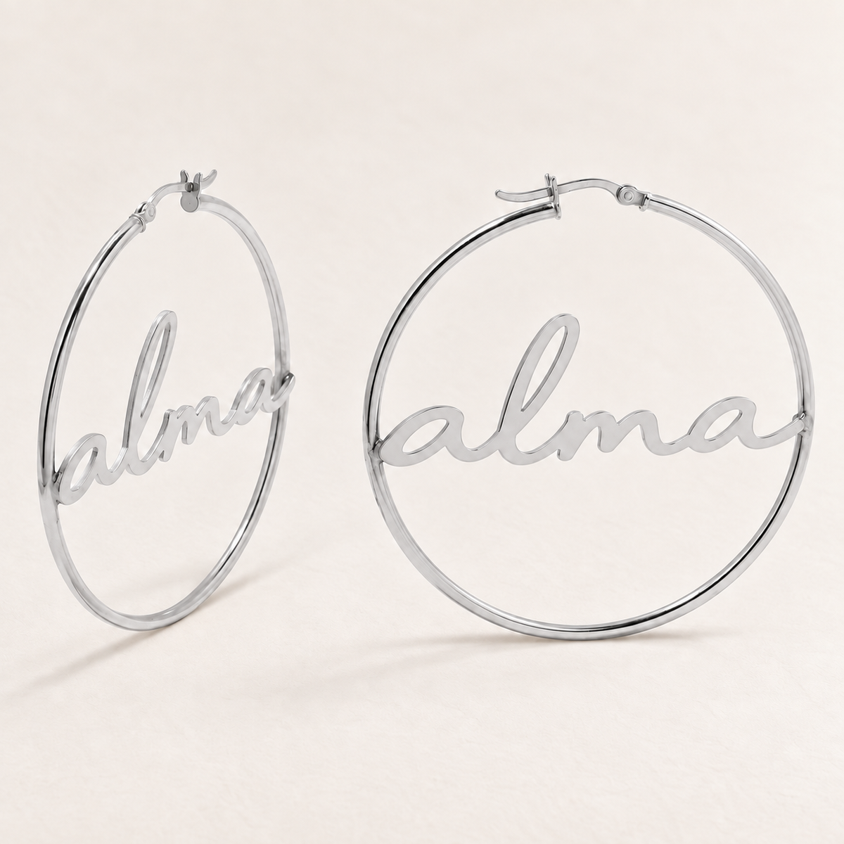 Custom Script Name Hoop Earrings hero photo - silver script name hoops on pale ivory Anthology Jewelry