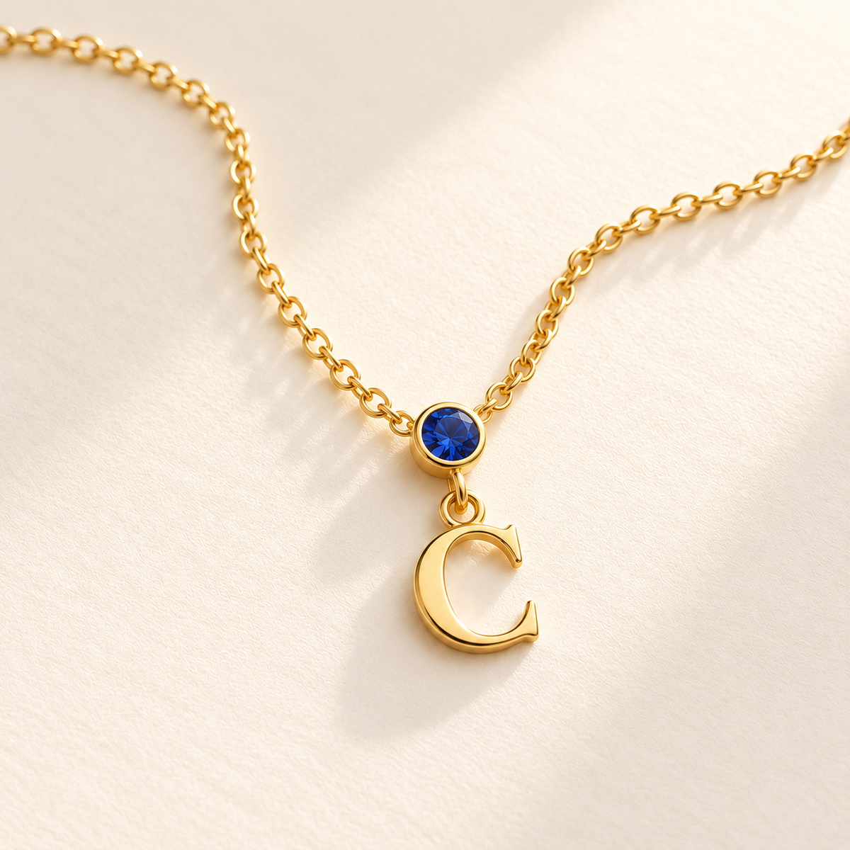 Gold vertical birthstone initial necklace on warm ivory surface