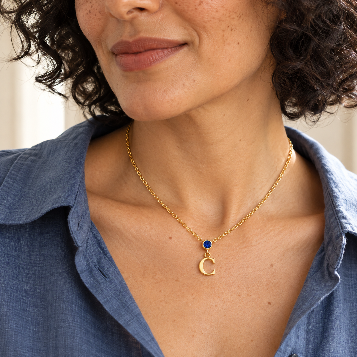 Woman in blue shirt wearing vertical birthstone initial necklace