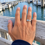 Custom Wide Band Name Ring with Birthstone UGC-style photo - silver Blue Topaz ring with Emma engraving on a relaxed hand at a harbor railing Anthology Jewelry