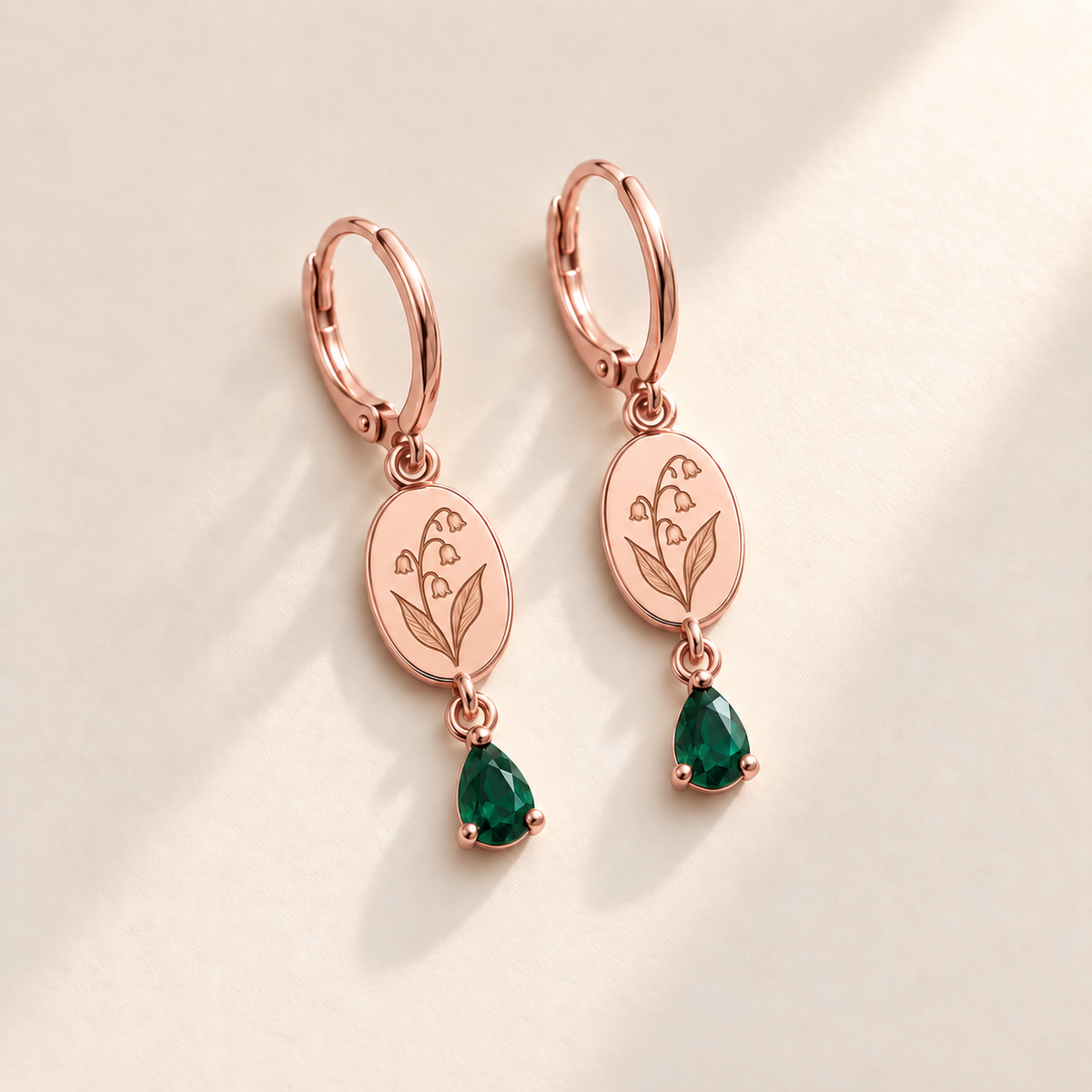 Custom Birth Flower & Birthstone Drop Earrings may rose gold hero photo - engraved four small downward lily-of-the-valley bells and two broad leaves with deep emerald green pear stones Anthology Jewelry