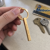 Casual phone photo of gold custom column keychain on a scratched desk