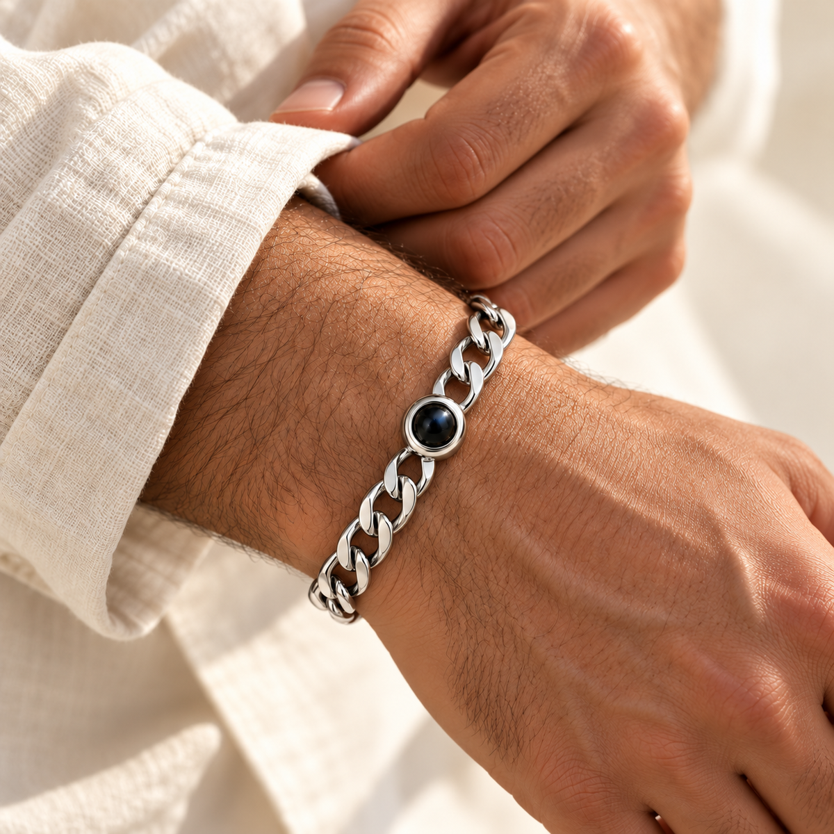 Custom Curb Link Photo Bracelet lifestyle photo - Silver photo bracelet worn while adjusting a pale linen cuff, with open oval curb links and dark projection lens - Anthology Jewelry