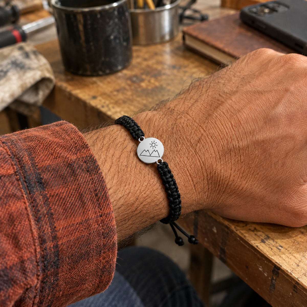 Custom Drawing Bracelet Men's Black Braided Cord lifestyle photo - silver disc with mountain and sun drawing on an adult wrist Anthology Jewelry