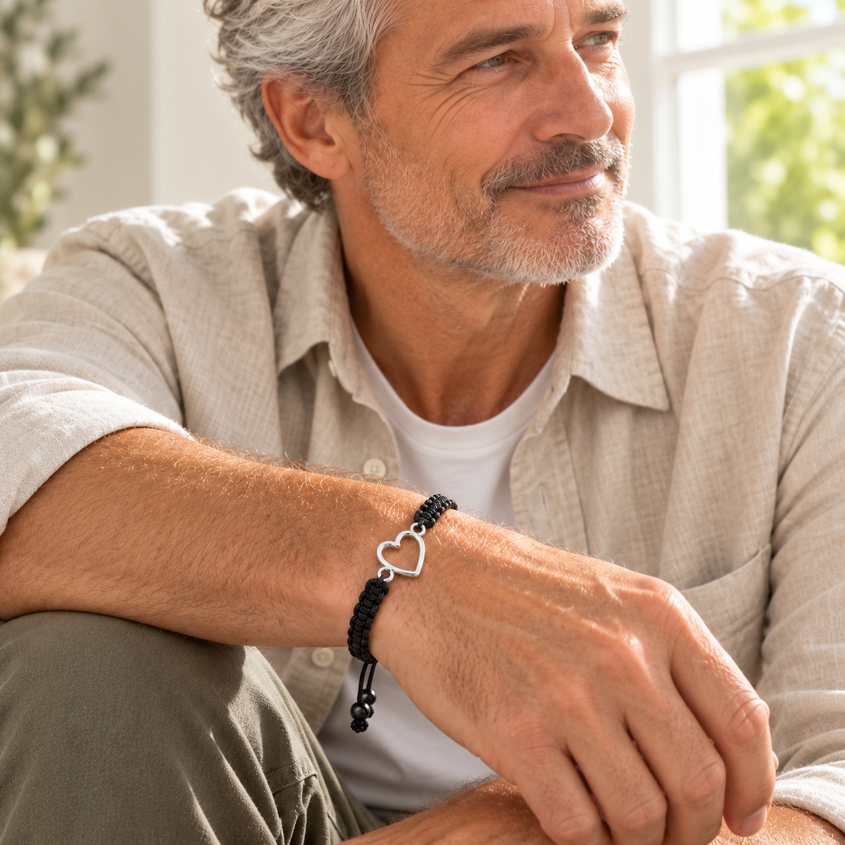 Custom Drawing Cutout Bracelet | Men's Black Braided Cord lifestyle photo - silver open heart outline bracelet worn by an adult man in a linen shirt, design concept Anthology Jewelry