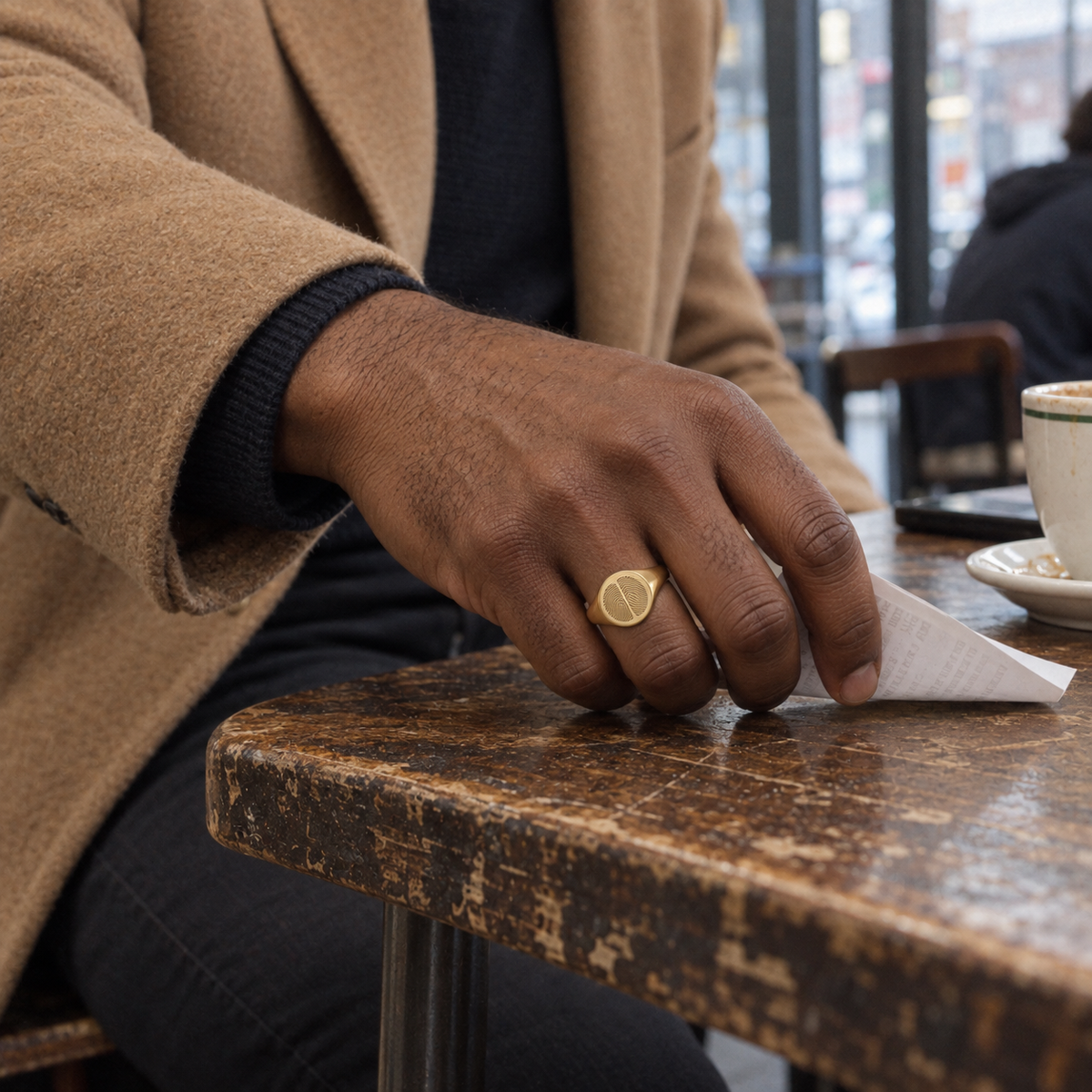 Custom Duo Fingerprint Signet Ring lifestyle photo - man wearing gold duo fingerprint signet ring at cafe table Anthology Jewelry