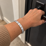 Custom Four-Stone Initial Bangle in silver with A / M personalization, worn at a door; illustrative phone-style marketing image - Anthology Jewelry