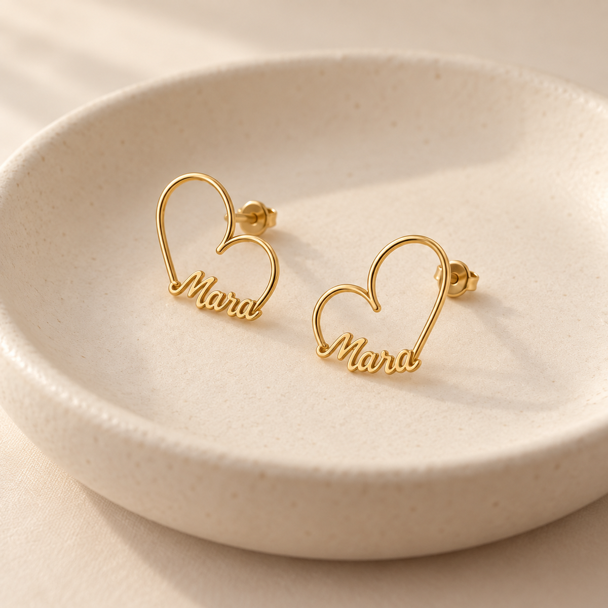 Custom Heart-Frame Name Stud Earrings gold pair in an ivory ceramic dish - Anthology Jewelry