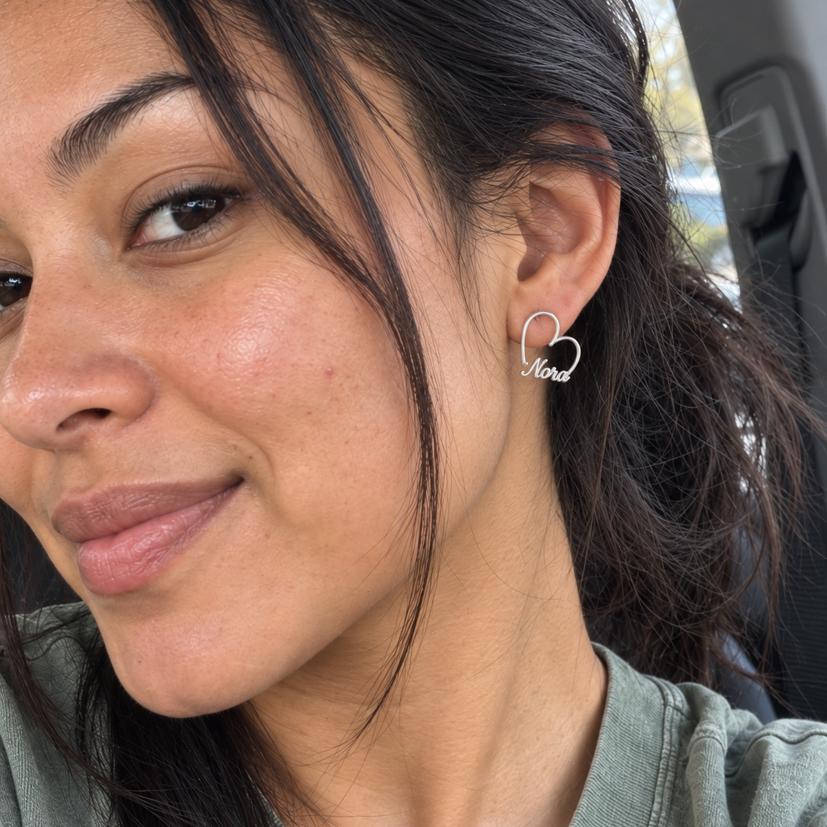 Custom Heart-Frame Name Stud Earrings in Silver, candid phone-style marketing image with Nora script name - Anthology Jewelry