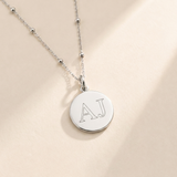 Custom Initials Necklace hero photo - sterling silver disc pendant engraved with two initials on cream background Anthology Jewelry