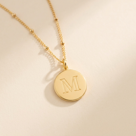 Custom Initials Necklace hero photo - gold engraved initial disc pendant on cream background Anthology Jewelry