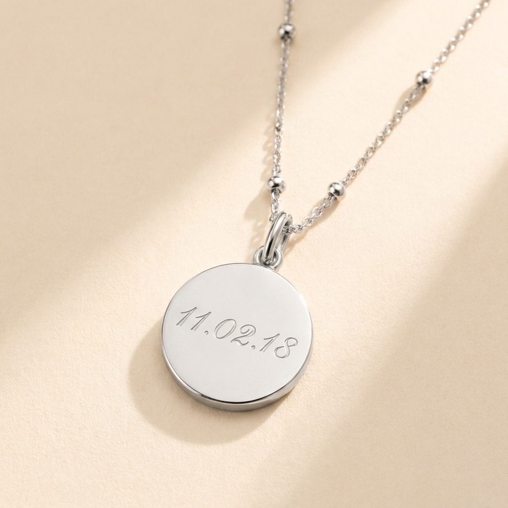 Custom Memorial Necklace hero photo - sterling silver disc pendant engraved with a date on cream background Anthology Jewelry