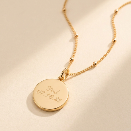 Custom Memorial Necklace hero photo - gold engraved name and date disc pendant on cream background Anthology Jewelry