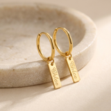 Custom Nameplate Huggie Hoop Earrings glamour photo - gold huggie hoop earrings styled on ceramic dish Anthology Jewelry