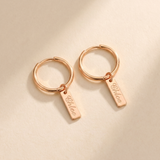 Custom Nameplate Huggie Hoop Earrings hero photo - rose gold huggie hoop earrings with engraved nameplate charm on cream background Anthology Jewelry