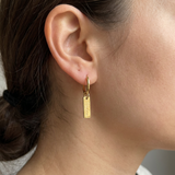 Custom Nameplate Huggie Hoop Earrings UGC photo - close up candid shot of gold huggie hoop earring Anthology Jewelry