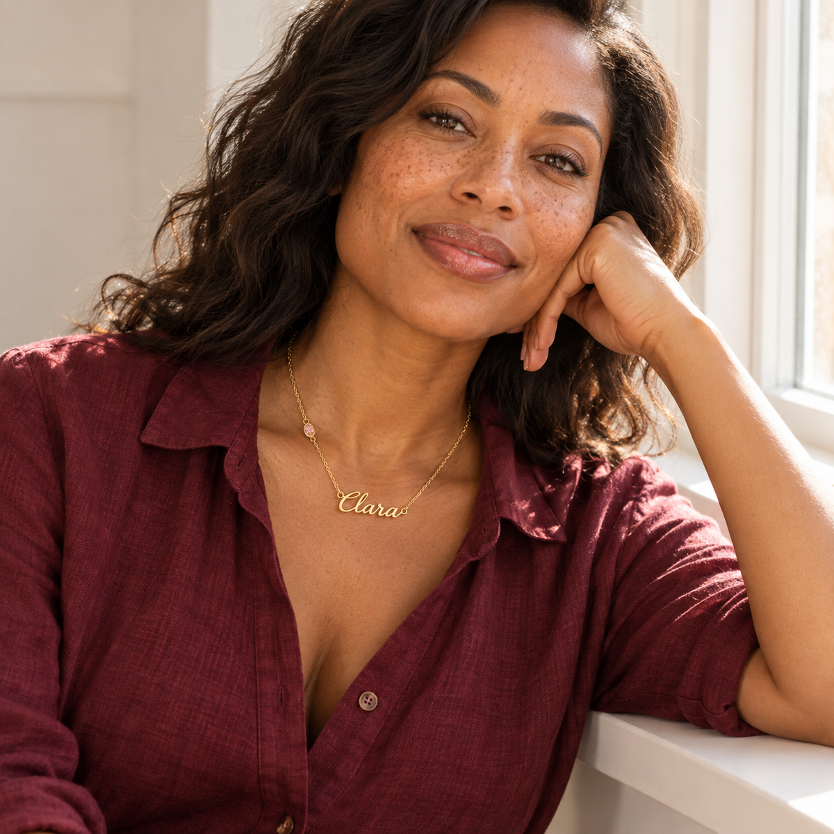 Woman in burgundy shirt wearing script name birthstone necklace