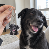 Casual phone photo of silver custom dog charm beside the pictured dog
