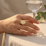 Custom Photo Locket Ring professional lifestyle photo - hand beside a glass of water on a linen table wearing gold oval hinged locket ring Anthology Jewelry