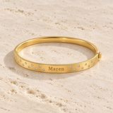 Gold hinged name bangle showing its engraved front and scattered stones