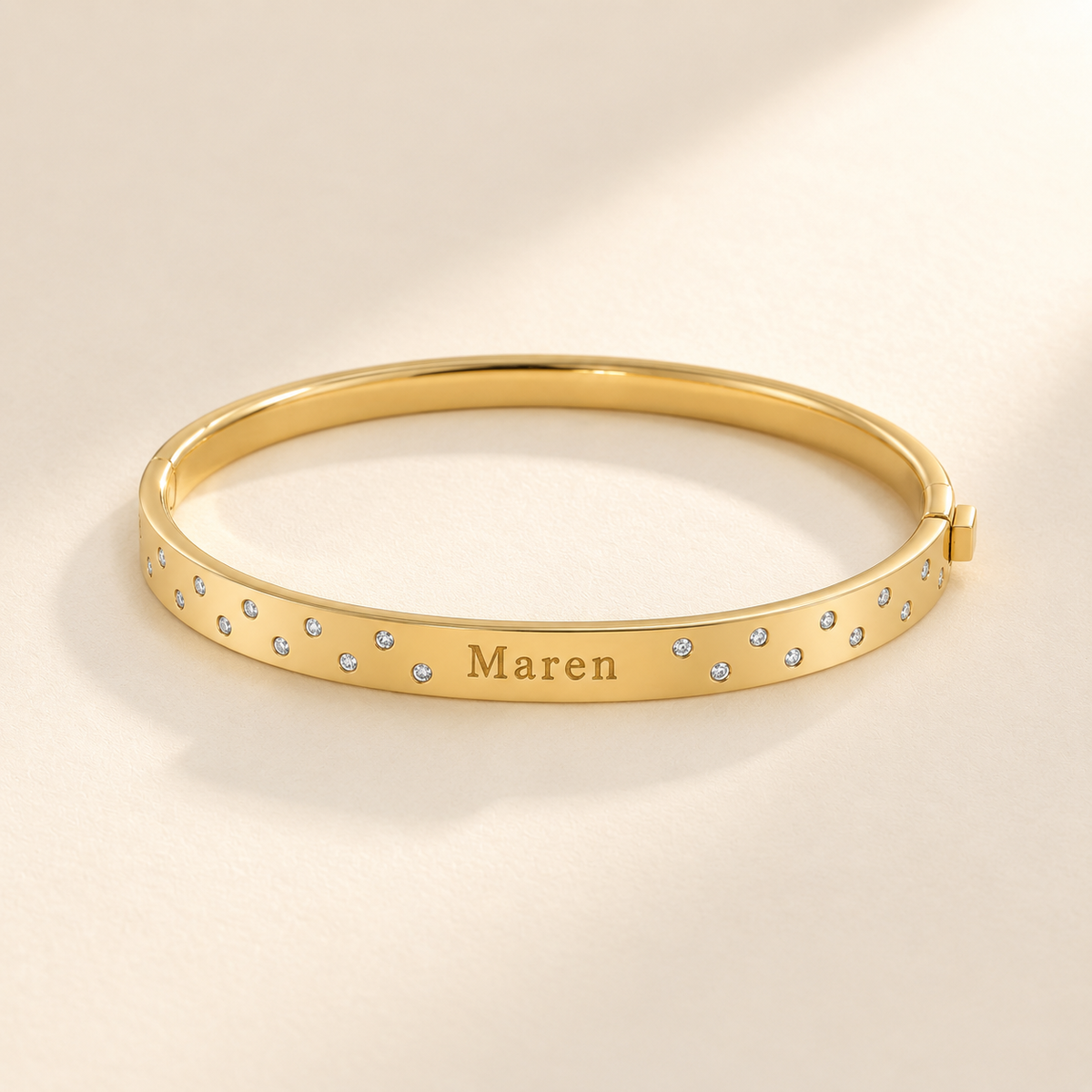 Gold scattered-stone name bangle with Maren engraving, viewed as a horizontal oval
