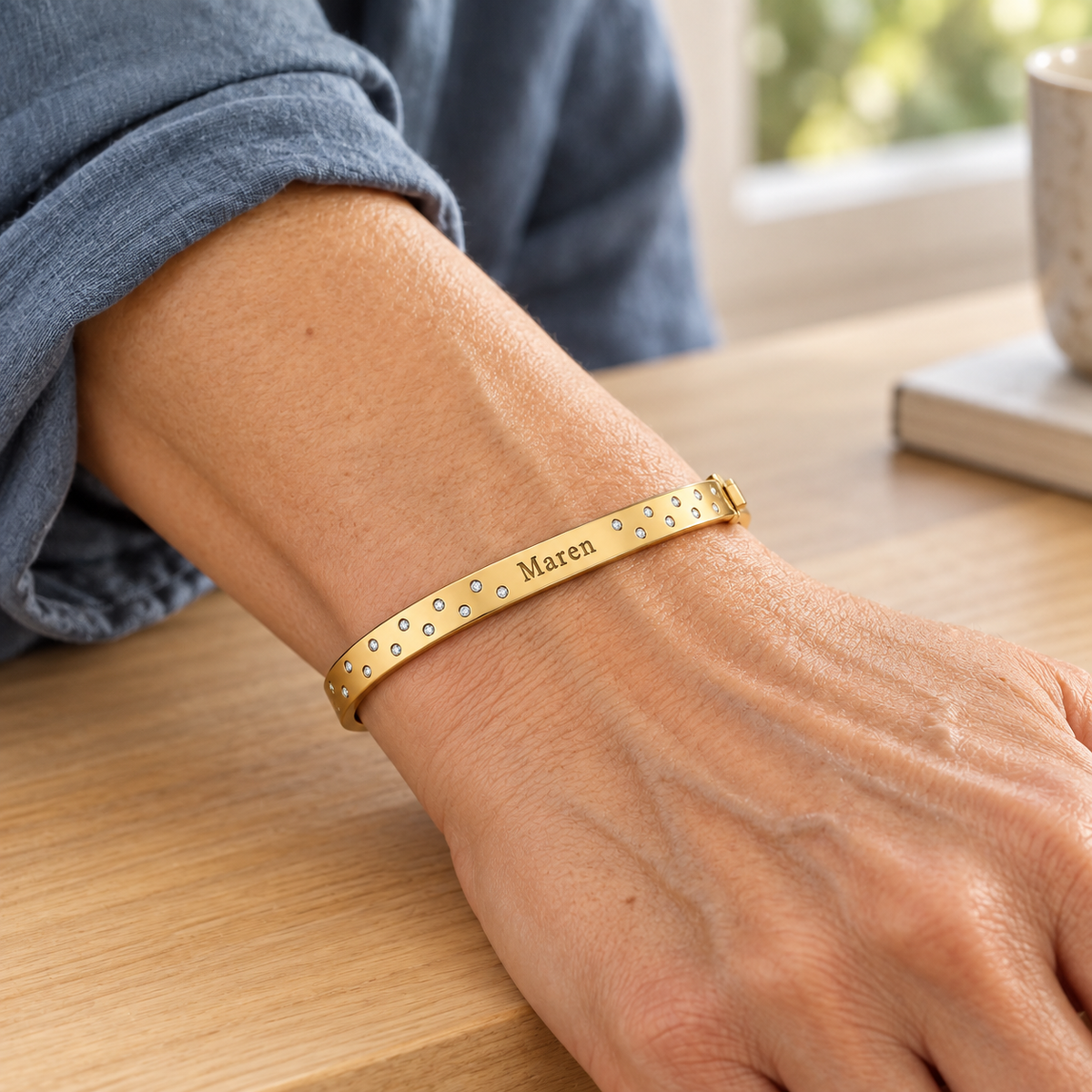 Scattered-stone gold name bangle worn at the wrist in a close editorial portrait