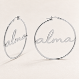 Custom Script Name Hoop Earrings hero photo - silver script name hoops on pale ivory Anthology Jewelry