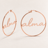 Custom Script Name Hoop Earrings hero photo - rose gold script name hoops on pale ivory Anthology Jewelry