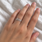 Custom Script Name Ring in silver with Nora personalization, casual phone-style worn view on white fabric - Anthology Jewelry