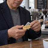 Custom Soundwave Money Clip lifestyle photo - man holding cash secured with gold soundwave money clip at cafe counter Anthology Jewelry