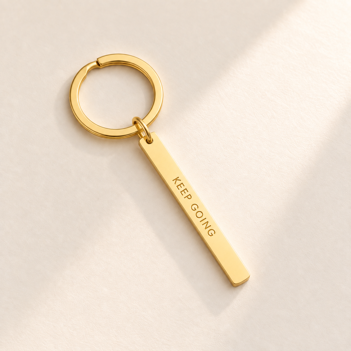 Custom Vertical Bar Keychain hero photo - gold engraved bar on pale ivory with soft top-right light Anthology Jewelry