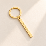 Custom Vertical Bar Keychain hero photo - gold engraved bar on pale ivory with soft top-right light Anthology Jewelry
