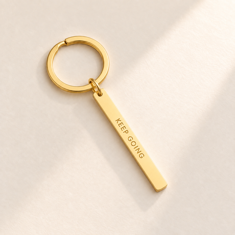 Custom Vertical Bar Keychain hero photo - gold engraved bar on pale ivory with soft top-right light Anthology Jewelry