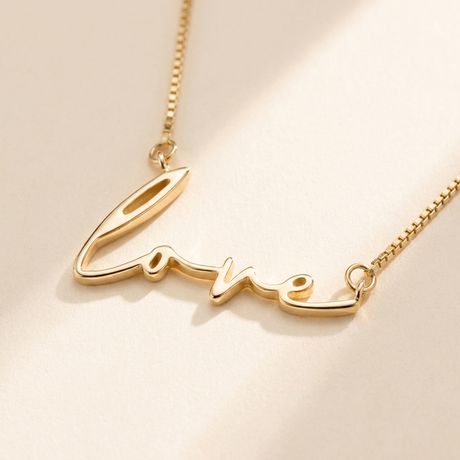 "Love" Necklace detail photo - close-up of polished gold script lettering Anthology Jewelry