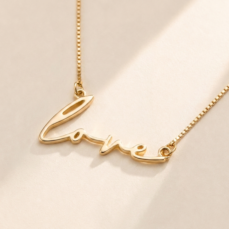 "Love" Necklace hero photo - gold script cutout pendant on cream background Anthology Jewelry