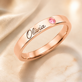 Name Ring with Birthstone (Classic Band) hero photo - rose gold flat band engraved with Olivia and a pink birthstone Anthology Jewelry